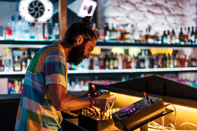 Side view dj spinning and mixing music at turntable during party in illuminated nightclub