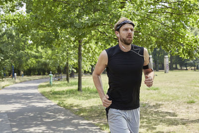 Man listening music while running against trees in park