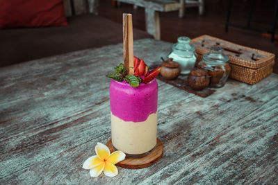 Smoothie in glass with straw, frangipani flower, sliced strawberry on wooden table. healthy dessert