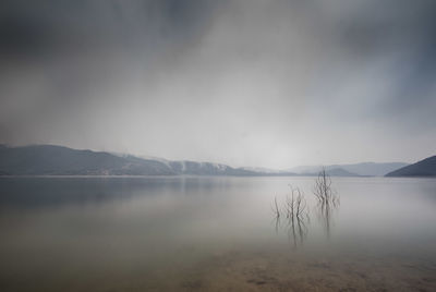 Scenic view of calm lake against sky during foggy weather