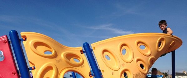 Boy on slide at park against sky