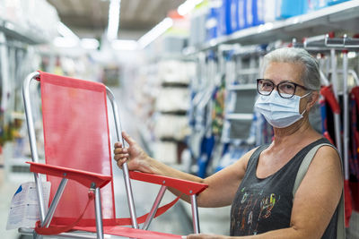 Portrait of senior woman with protective face mask holding chair in store