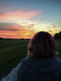 Rear view of woman on field against sky during sunset