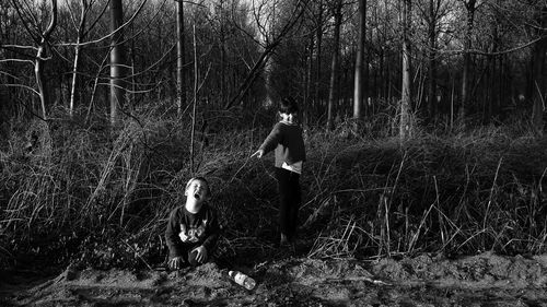 Smiling girl standing by plants and crying brother sitting in forest