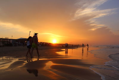 People walking at beach against sky during sunset