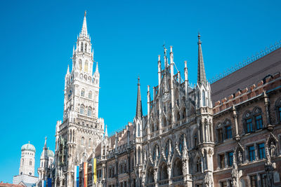 Low angle view of new town hall by munich cathedral against clear blue sky