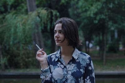 Close-up of thoughtful teenage girl smoking cigarette against trees