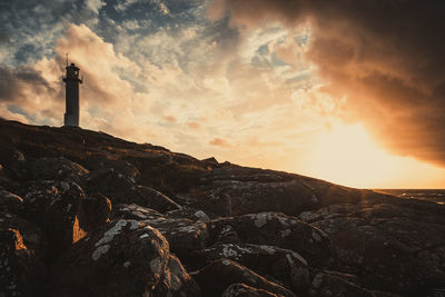 Lighthouse on rock against sky during sunset