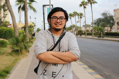 Portrait of young man standing by palm trees in city