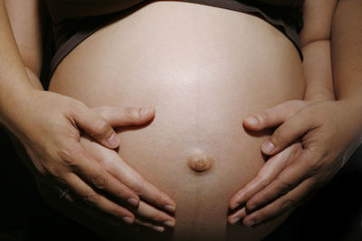 Cropped hands of couple touching belly against black background