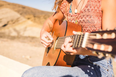 Midsection of woman playing guitar against mountain