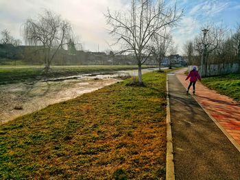 Rear view of woman skating on footpath by river