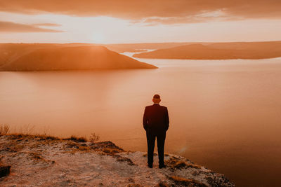 Rear view of man walking on mountain against sky during sunset