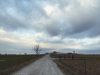 Road passing through field against cloudy sky