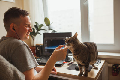 Smiling man playing with cat while working at home