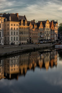 Buildings reflecting in canal at town against sky