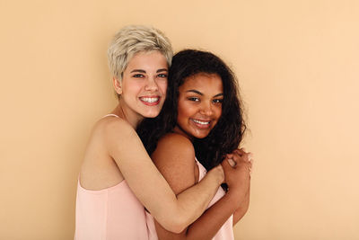 Side view portrait of smiling friends embracing against beige background