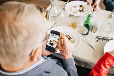 Senior man taking picture of food in restaurant