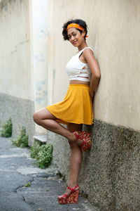 Portrait of smiling young woman standing against wall