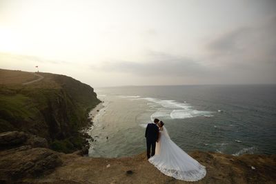 Rear view of bride and groom on cliff against coastline and sky