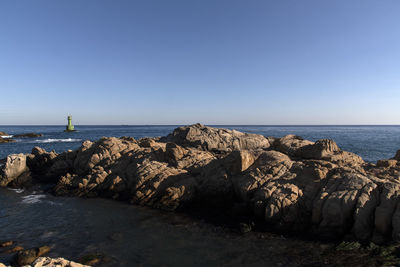 Rocks by sea against clear blue sky