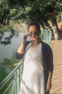 Portrait of young woman wearing sunglasses while standing against lake