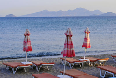 Chairs and tables on beach by sea against clear sky