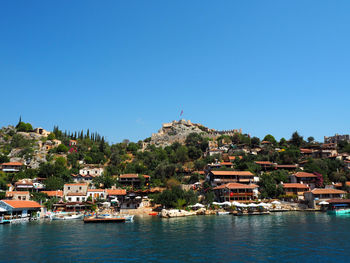 Buildings by lake against clear blue sky