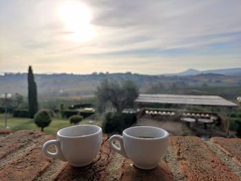 Close-up of coffee cup against sky at sunset