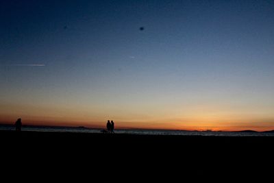 Silhouette people on beach against clear sky during sunset