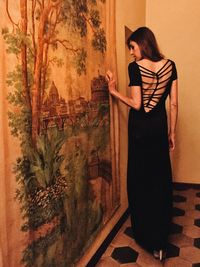 Full length rear view of beautiful woman walking by painting on wall