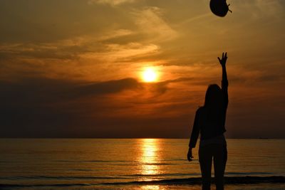 Silhouette of woman standing at beach against sky during sunset