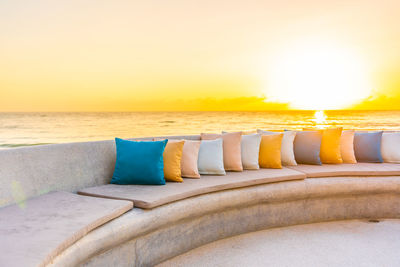 Lounge chairs by swimming pool at beach against sky during sunset