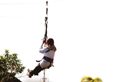 Low angle view of young woman hanging on tree against clear sky