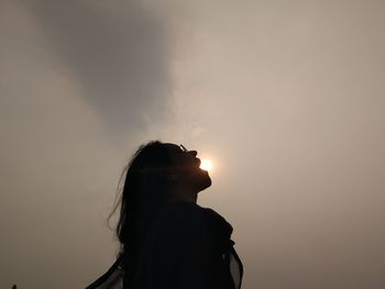 Optical illusion of woman eating sun against sky during sunset