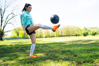 Full length of young woman playing soccer on field against sky