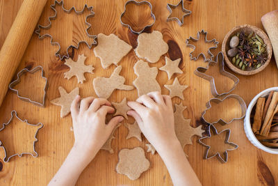 Children with their mother cut out christmas gingerbread cookies on the table from rolled dough. 