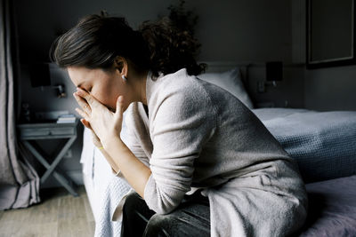 Side view of lonely anxious woman sitting by bed at home