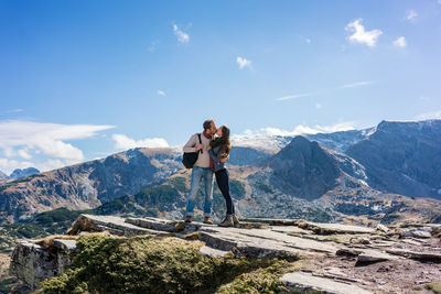 Couple kissing while standing against mountain during sunny day