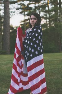 Portrait of girl wrapped in american flag while standing on field