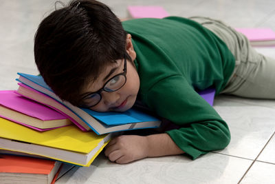 Boy wearing eyeglasses lying on book over floor