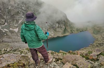 Rear view of man with ice axe standing by lake and mountains