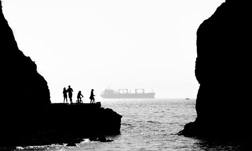 Silhouette people standing on rock by sea against clear sky
