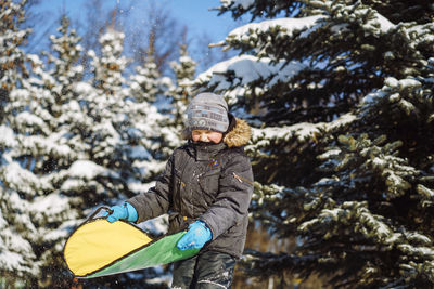 Cute caucasian boy holding a snow saucer to slide from hill in winter park