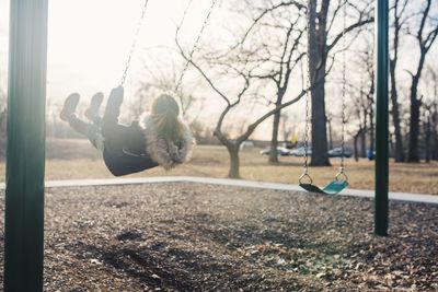 Young woman swinging against sky at park