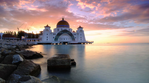 View of building by sea against sky during sunset