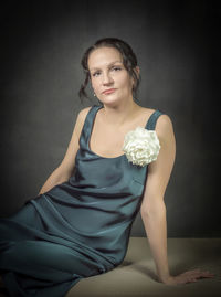 A beautiful girl in an evening gown is sitting against a gray wall