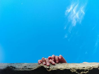 Cropped hands on retaining wall against blue sky