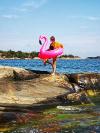 Side view of man on rock at beach against sky