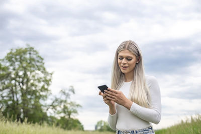 Young woman using mobile phone against sky